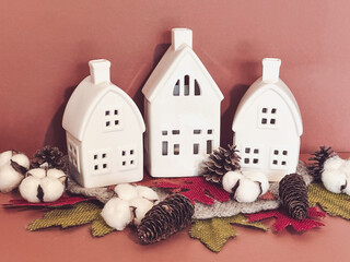 Three  white ceramic village houses styled with cotton bolls, pinecones, felt, and burlap leaves in a bright Scandinavian inspired autumn still life. Thanksgiving or Halloween Decoration © Ryan