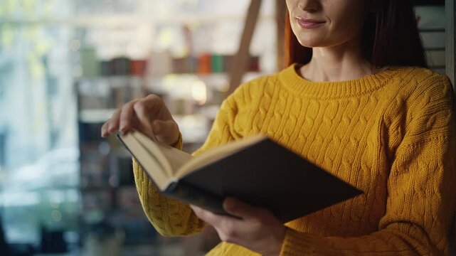 Smiling young woman reading in a bookshop, self-education and reading hobby