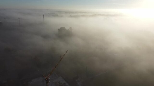 Aerial sunset landscape. Cloud fog covering misty land. Morning fog covering forest at misty sunrise. Treetop with power lines and wind turbines peek through sunset fog. Sunrise fog aerial footage