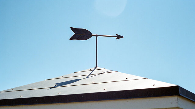 Vintage arrow weather vane on roof pointing direction against clear blue sky