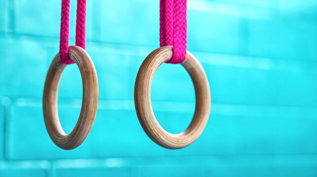 Wooden gymnastics rings with pink straps against turquoise wall background