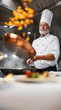 Elderly caucasian male chef saut&eacute;ing vegetables in professional kitchen