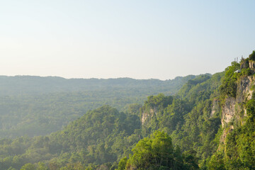 Fototapeta premium A scenic aerial view of a steep rocky cliff covered in green trees amidst a vast tropical forest.