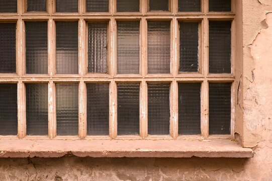 Old abandoned window with grid wooden frame weathered ledge and peeling plaster on wall