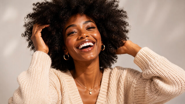 Radiant woman with curly afro hair laughing in a beige sweater