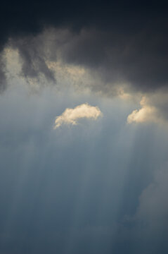A dramatic cloud edge reveals bright sunbeams and Tyndall rays breaking through the sky, capturing the tense calm just before the storm.