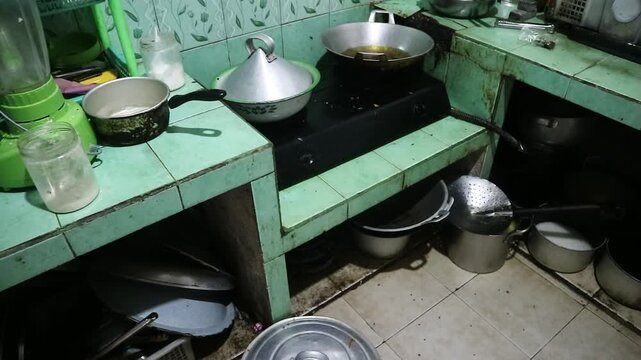A cluttered traditional kitchen interior with various cooking pots and pans on a tiled counter, dirty and messy