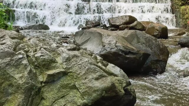 Cascading tiered waterfalls flowing through a rocky riverbed surrounded by natural stone formations in a serene forest setting