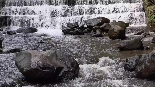 Serene cascading waterfall flowing over weathered rocks amidst lush greenery, a peaceful natural landscape