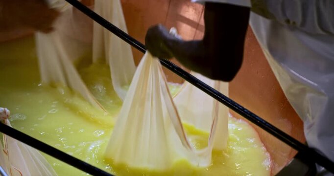 Slow Motion Of Dairy workers stretching long sheets of elastic cheese curd across metal rods during traditional production. Cheesemakers Stretching Elastic Curd over Copper Vat