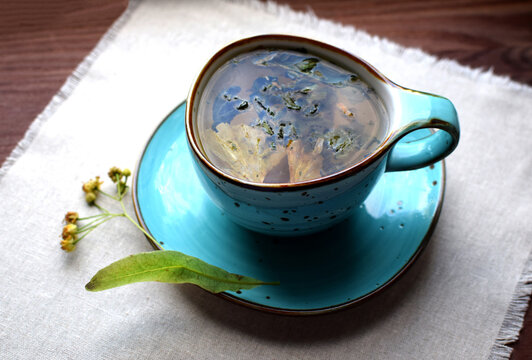 Herbal green tea with dried ginkgo biloba leaves and linden in a blue ceramic cup on a cloth napkin.