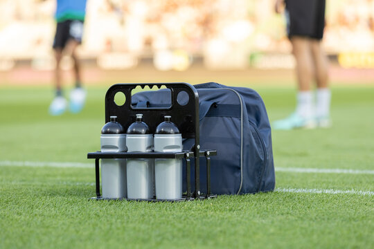 Soccer Hydration. Sport bottles of fresh water or energy drink on a soccer, football field. Players and Balls on Background