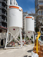 Large White Cement Silos at Urban Construction Site with Modern Buildings. Urban Apartment Buildings © dechevm