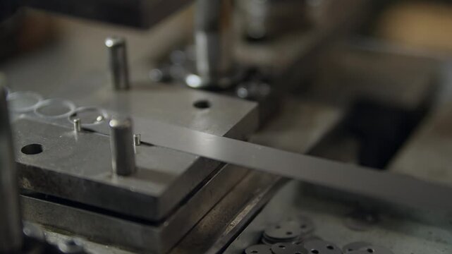 Worker adjusts metal mold with gloved hands. Machine hovers above coins ready for pressing. Tooling shows industrial precision in a factory. Scene captures manufacturing focus and craftsmanship