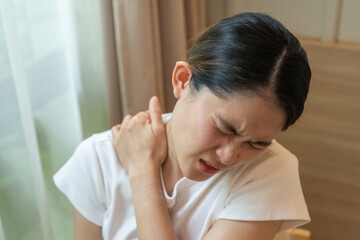 Fototapeta premium Cropped shot view of Asian woman having shoulder and neck pain from working longtime. Shoulder pain is when rotator cuff tendons become inflamed or trapped in your shoulder.