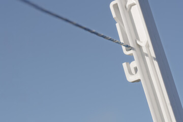 Electric Fence Wire Attached to a White Plastic Insulator Against Blue Sky © SynchR