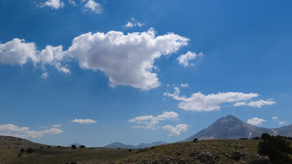 Mountain peaks and rugged terrain stretching out beneath a partly cloudy, clear blue sky. A perfect stock image for themes of freshness and the great outdoors. © TAMER YILMAZ