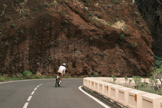 A lone cyclist gracefully navigates a dramatic winding road, bordered by an imposing red mountain landscape. Capturing the essence of outdoor sport, endurance, and exploration.