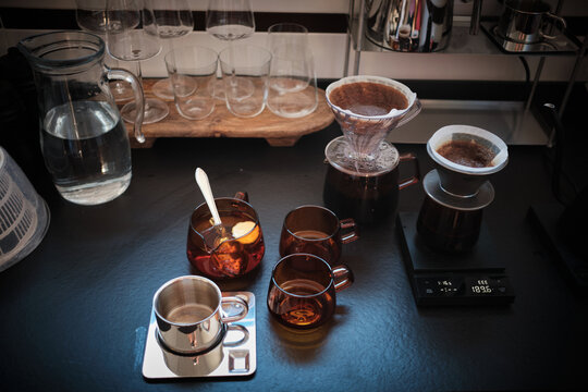 Modern coffee and tea brewing station with pour-over drippers, elegant glassware, a water pitcher, and a precision scale on a sleek dark counter, ready for a fresh brew.