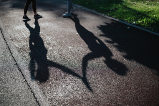 Two people running and holding hands, their elongated shadows stretched across a textured track. A couple jogging together on a sunlit path, captured as dark silhouettes on the pavement.