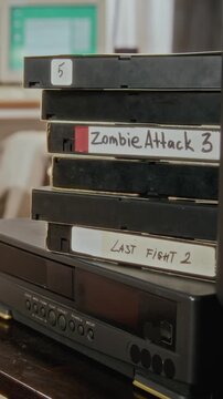 Vertical shot of vintage VHS tapes stacked on retro VCR player with handwritten labels. Footage is ideal for media digitization services or nostalgia-themed marketing campaigns