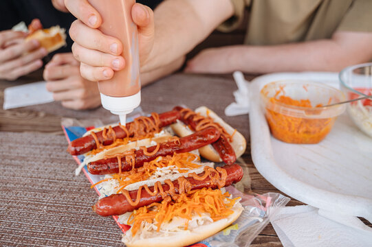 Hand pouring rich savory sauce over a grilled sausage in a hot dog topped with Korean-style spicy carrots, street food