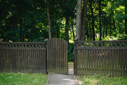 Rustic wooden fence with an open gate leading into a lush green public park, inviting landscape concept