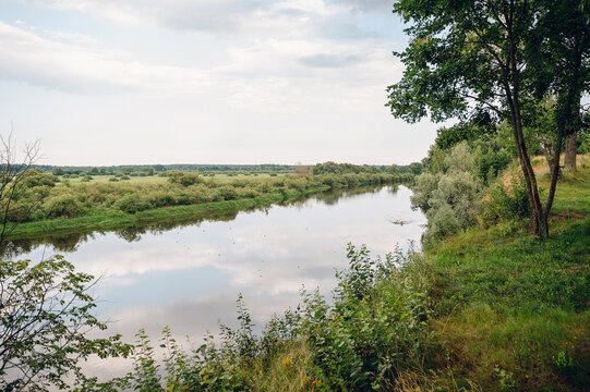 Wide scenic river with quiet current and dense wooded banks under a gloomy overcast sky, peaceful nature landscape