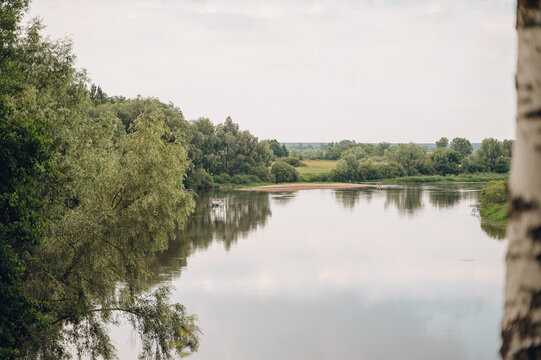 Wide scenic river with quiet current and dense wooded banks under a gloomy overcast sky, peaceful nature landscape