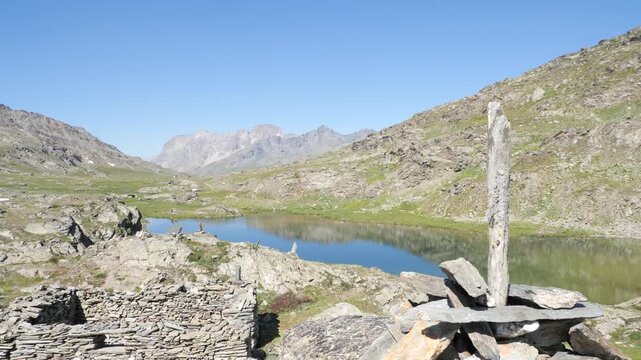 Crystal clear alpine lake reflecting rugged mountain peaks beneath cloudless blue sky in Italian Alps, showcasing pristine wilderness, tranquil waters and spectacular summer scenery