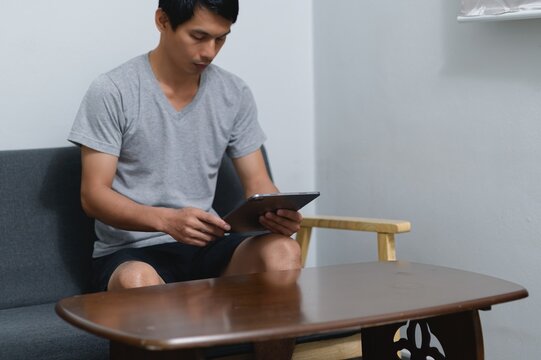 Young Man Sitting on Sofa Using Tablet in Cozy Living Room Setting