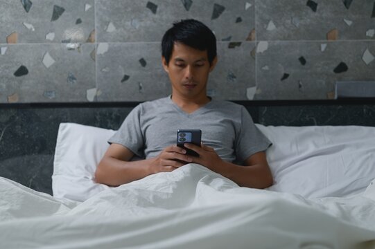 Man Sitting on Bed Using Smartphone in Cozy Bedroom Setting