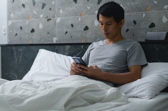 Young Man Sitting on Bed Using Smartphone in Modern Bedroom