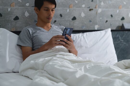 Young Man Relaxing in Bed Using Smartphone in Cozy Indoor Space