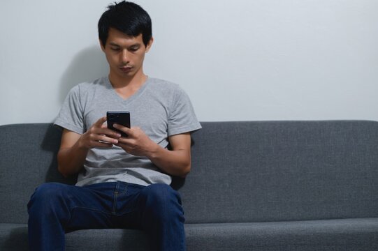 Young Man Sitting on Couch Using Smartphone in Modern Living Room