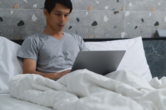 Focused Man Working on Laptop in Bed with Cozy White Blankets