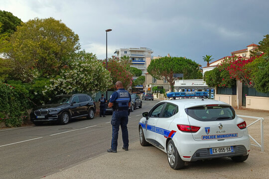 A French municipal police patrol on a street in Antibes, France, June 22, 2023. A uniformed officer stands on the side of the road next to a Renault Clio patrol car. A parking ticket has been issued