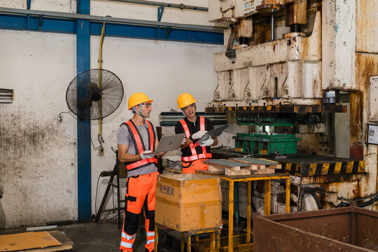 Engineers discussing production near heavy stamping press marked B1 in metal factory