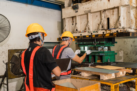 Workers examining green stamping die on industrial punch press from behind