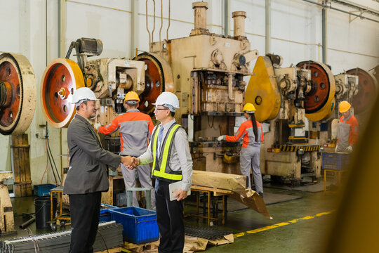 Engineer And Senior Manager Standing Beside Idle Stamping Press Discussing Factory Operations