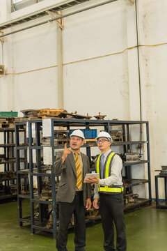 Factory Manager And Safety Engineer Pointing Upward Beside Steel Mold Storage Shelves