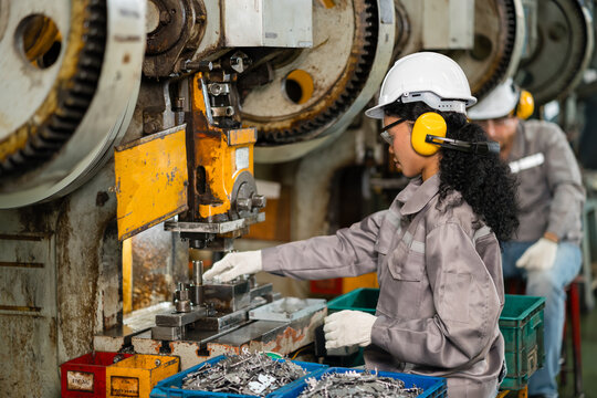 Female machine operator loading part into power press with coworker in background