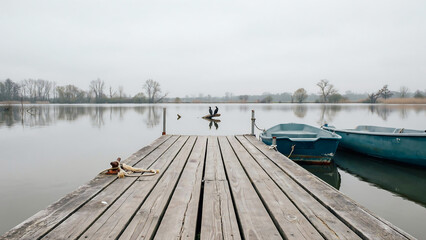 Fototapeta premium Wooden pier extending into a calm lake with moored blue boats isolated on a transparent background