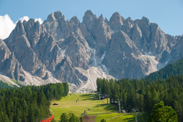 Dramatic Dolomites peaks near San Candido, Italy, with alpine forest, ski lift and green meadow under a clear blue sky. Stunning mountain landscape for travel and nature themes. © giemmephoto