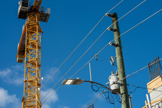 Construction crane and utility pole with power lines against blue sky