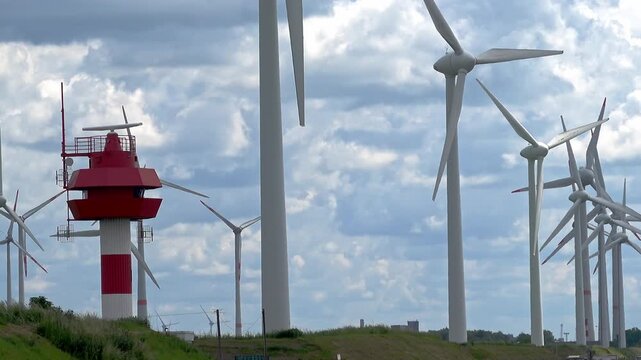 Coastal radar tower with rotating antenna and large wind turbine farm generating clean renewable energy on a cloudy day