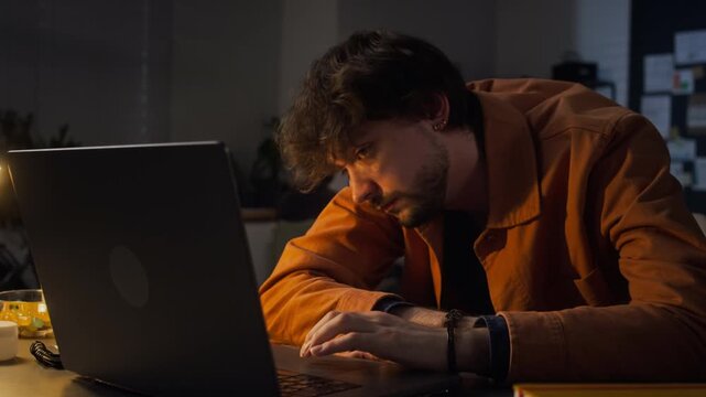 Caucasian young adult male office worker typing on laptop at night, feeling exhausted and falling asleep with head on keyboard. Suitable for corporate wellness and mental health campaigns