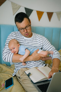 Father multitasking while remote working at home, holding his baby, balancing paternity leave, work, and family responsibilities, experiencing daily challenges and pressures
