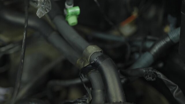 Close-up of black rubber fuel hoses inside messy car engine bay.