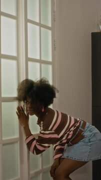 Vertical video of young adult Black woman and Caucasian man listening at door, getting scared by spooky shadow hand, and running away in panic. Ideal for comedy sketches or security commercials